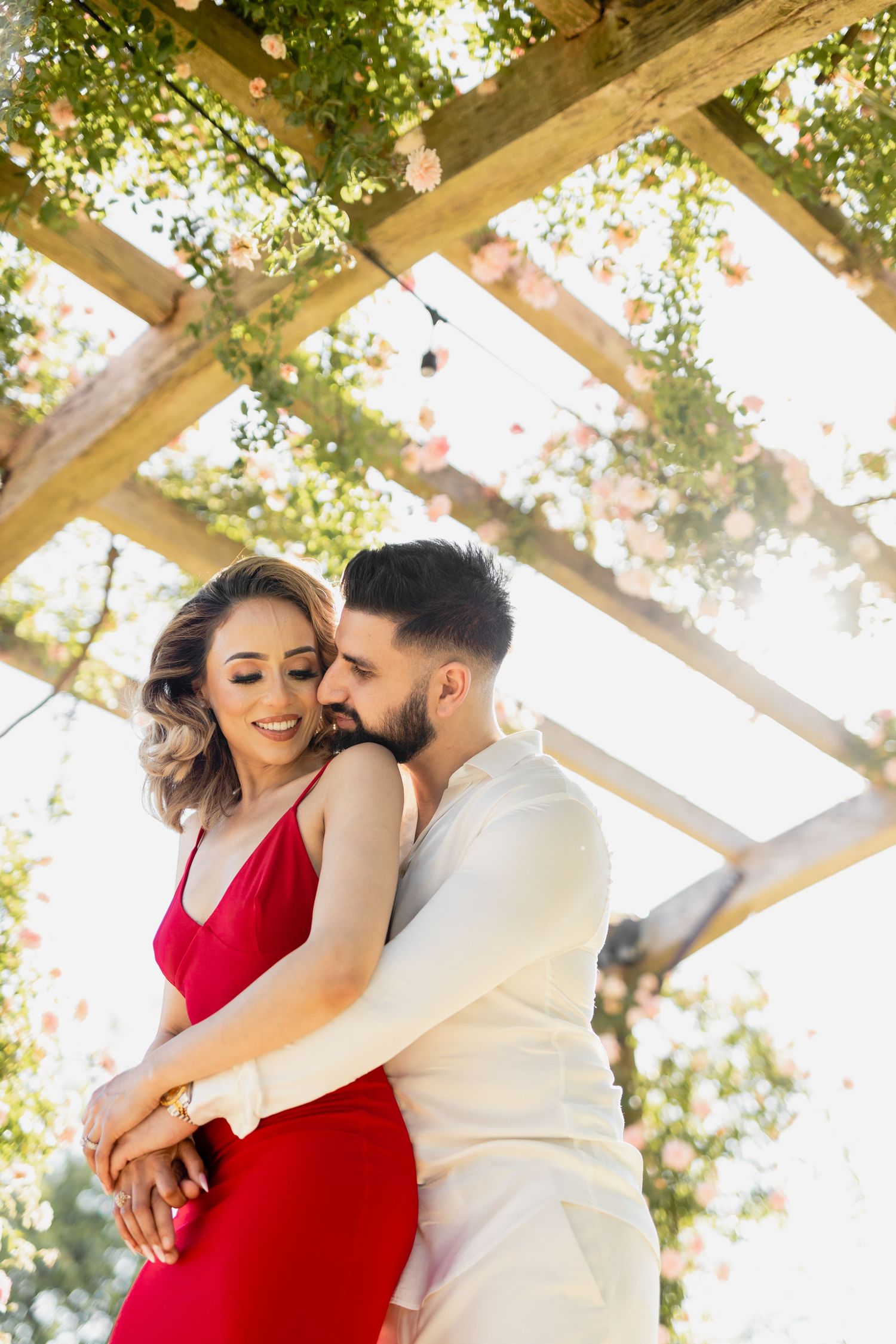 Inda and Sandie pre-wedding shoot – couple embracing under romantic floral pergola with string lights, woman in red dress outdoors, Indian