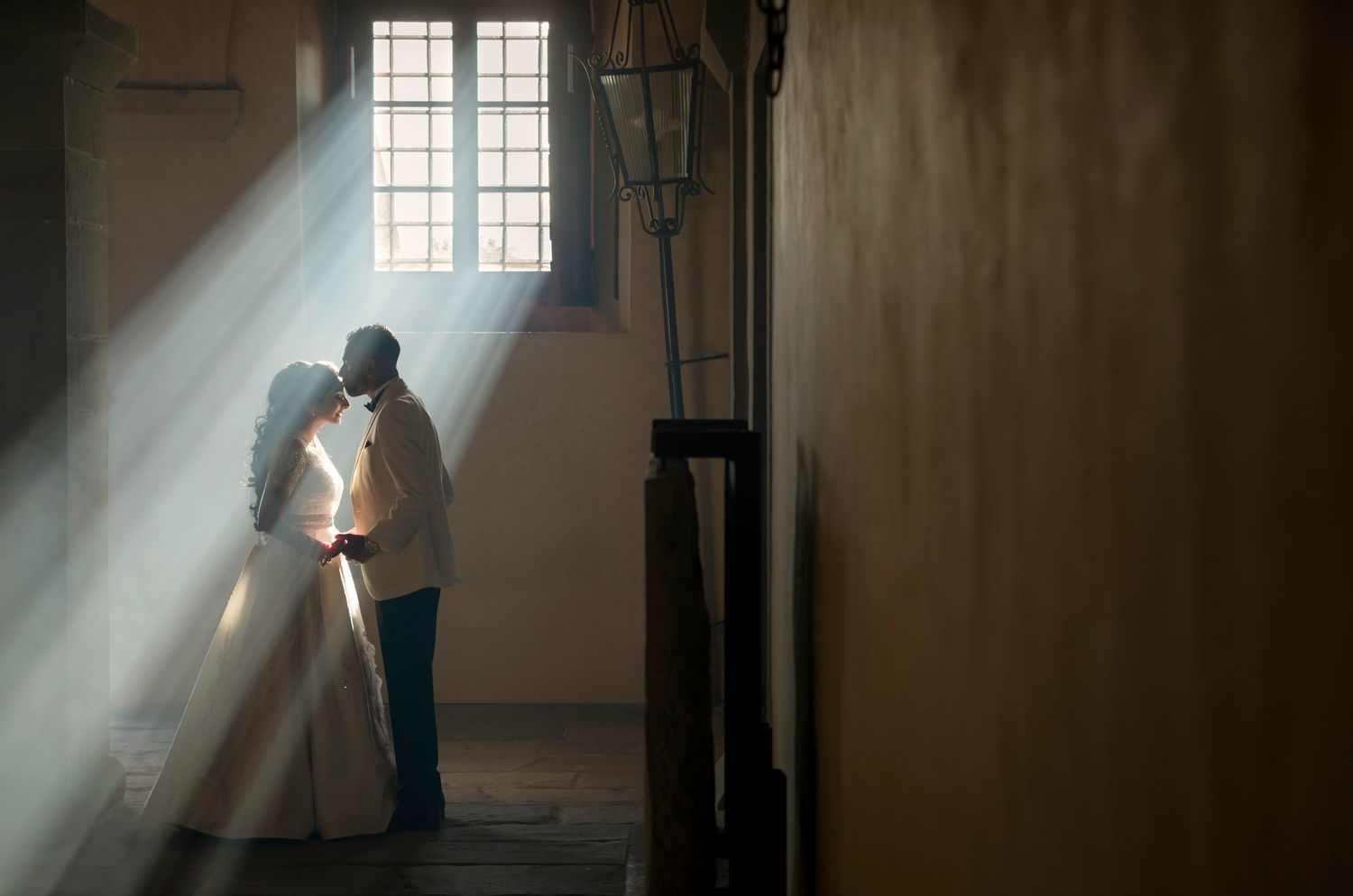 Guv and Amrita Sikh wedding – couple sharing intimate kiss in dramatic rays of light streaming through window in rustic historic venue, Sikh