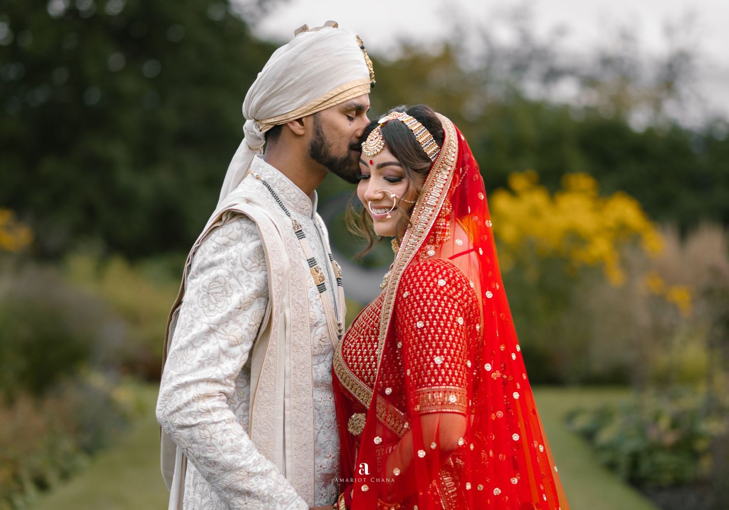 Akshay and Sherali Sikh wedding – Hindu couple sharing romantic moment outdoors in lush garden, bride in red lehenga, groom in sherwani