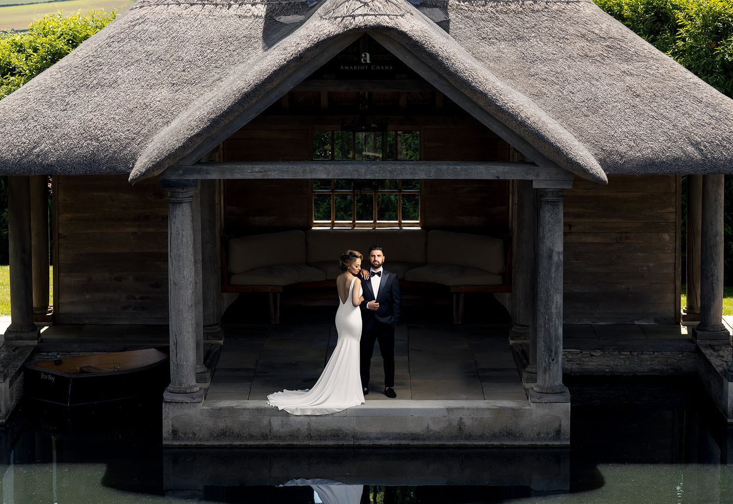 Inda and Sandie pre-wedding shoot – couple standing beneath thatched pavilion reflected in still water at dusk, luxury Indian wedding photo
