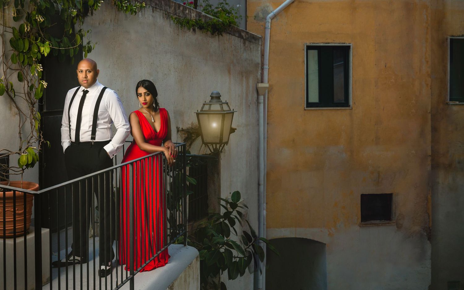 Amalfi pre-wedding portraits – elegant couple on Mediterranean balcony at dusk, woman in red gown, cinematic destination