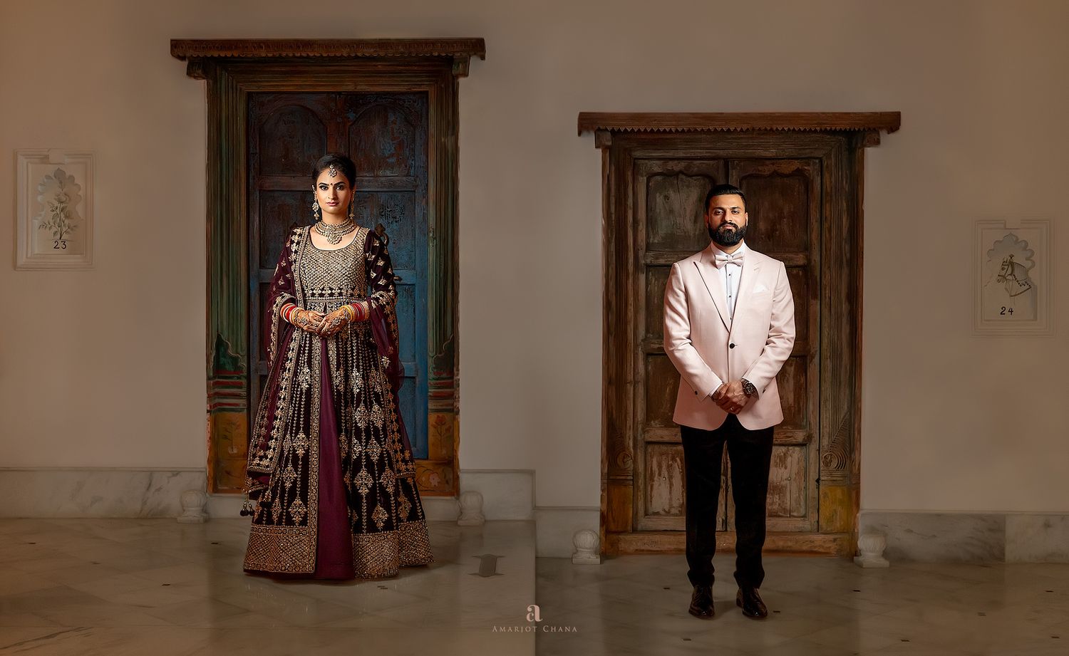 Indian couple in traditional and formal attire standing before ornate wooden doorways in an elegant gallery setting.