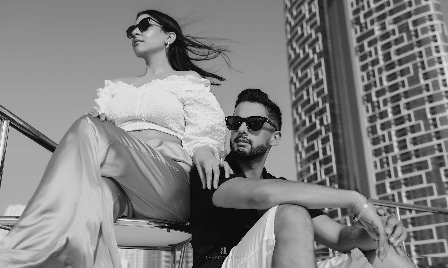 Stylish couple posing outdoors in black and white, woman in white blouse and man in sunglasses.