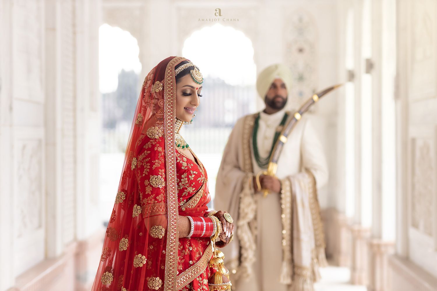 Raj and Benita Sikh wedding – bride in red and gold bridal lehenga with dupatta walking with groom in traditional turban in marble corridor,