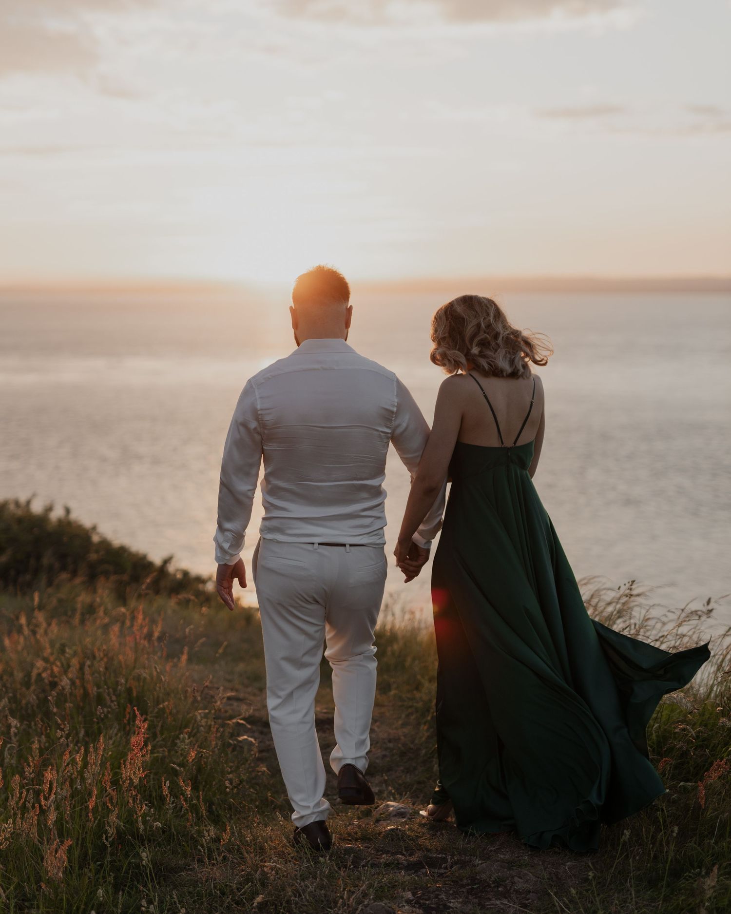 Inda and Sandie pre-wedding portraits – couple walking hand in hand toward golden ocean sunset, woman in flowing green gown, cinematic