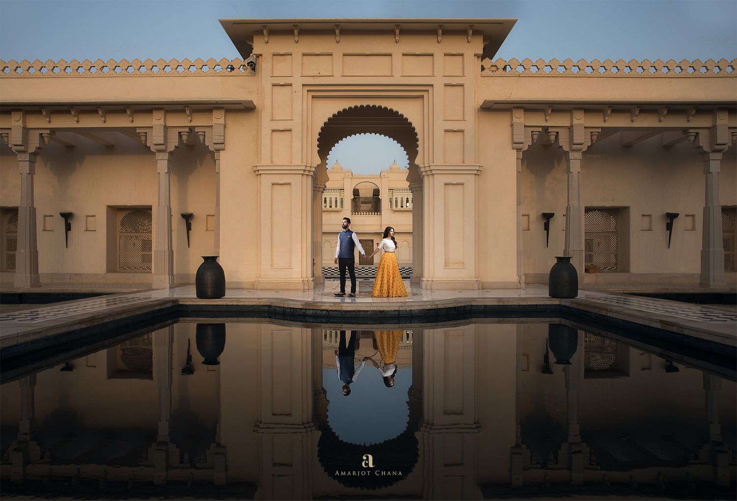 Couple reflected in still pool before a grand arched entrance of a Rajasthani heritage palace.