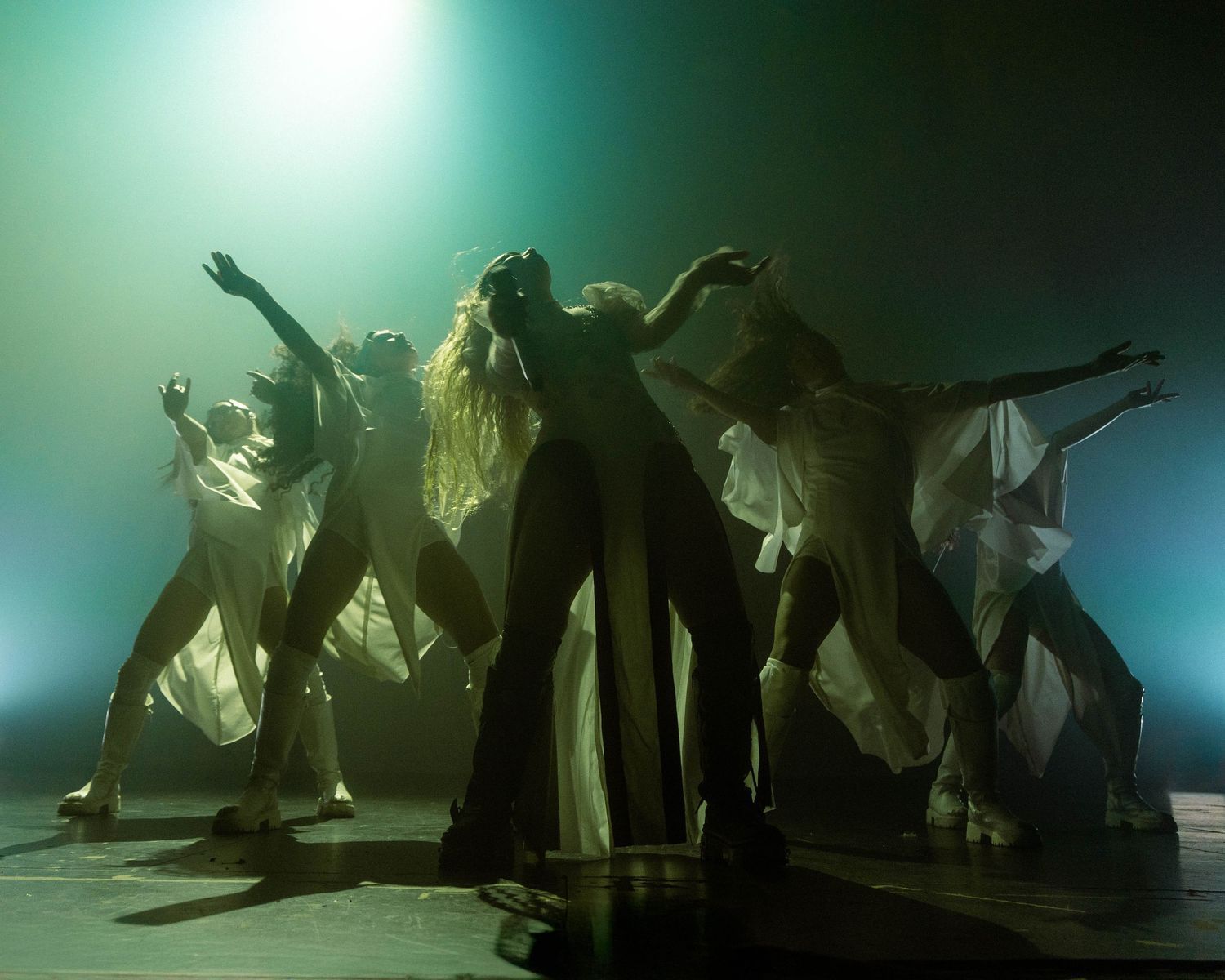 Silhouetted figures performing an artistic dance routine in ethereal green lighting.