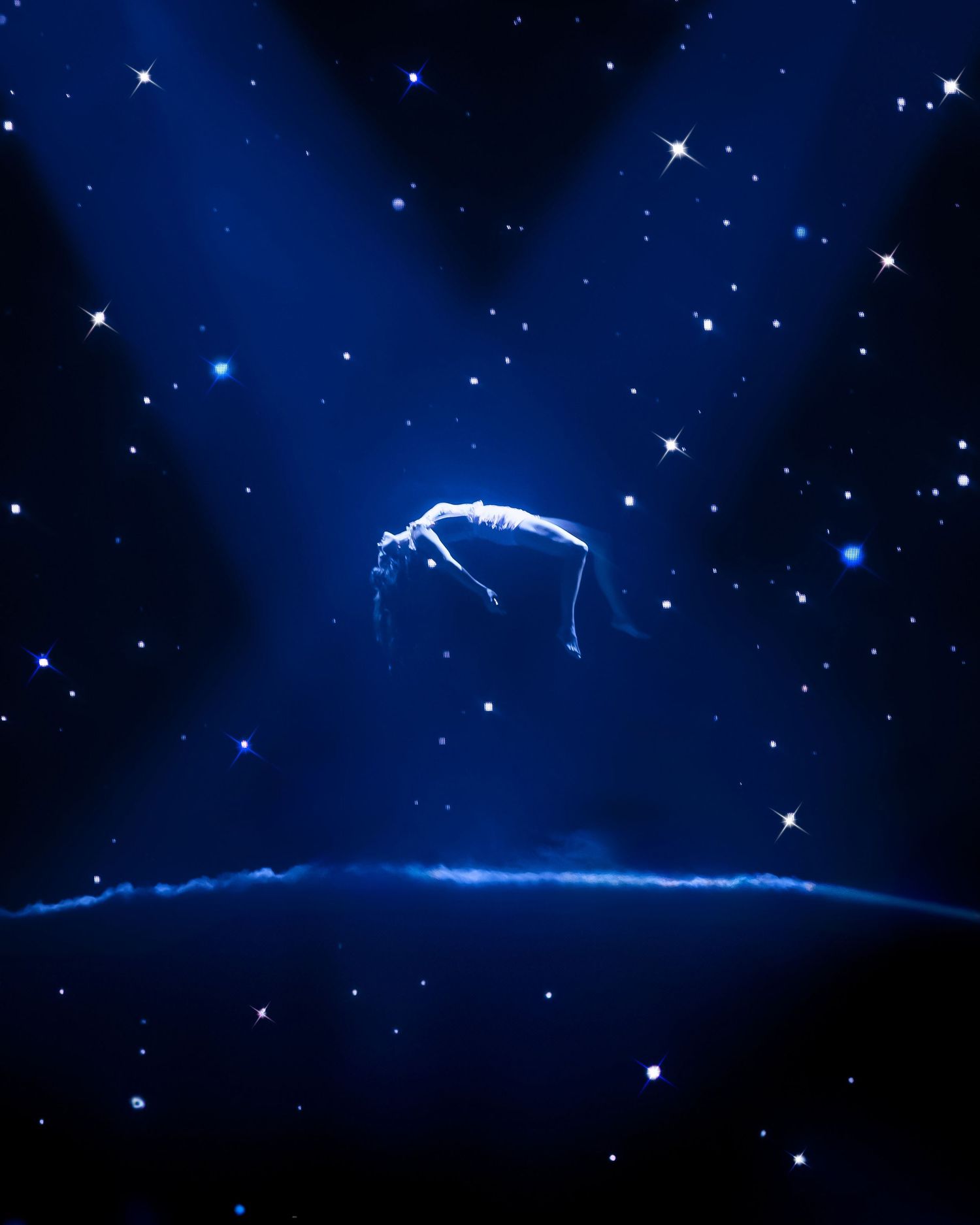 Artistic silhouette of performer floating against starry blue backdrop during stage performance.