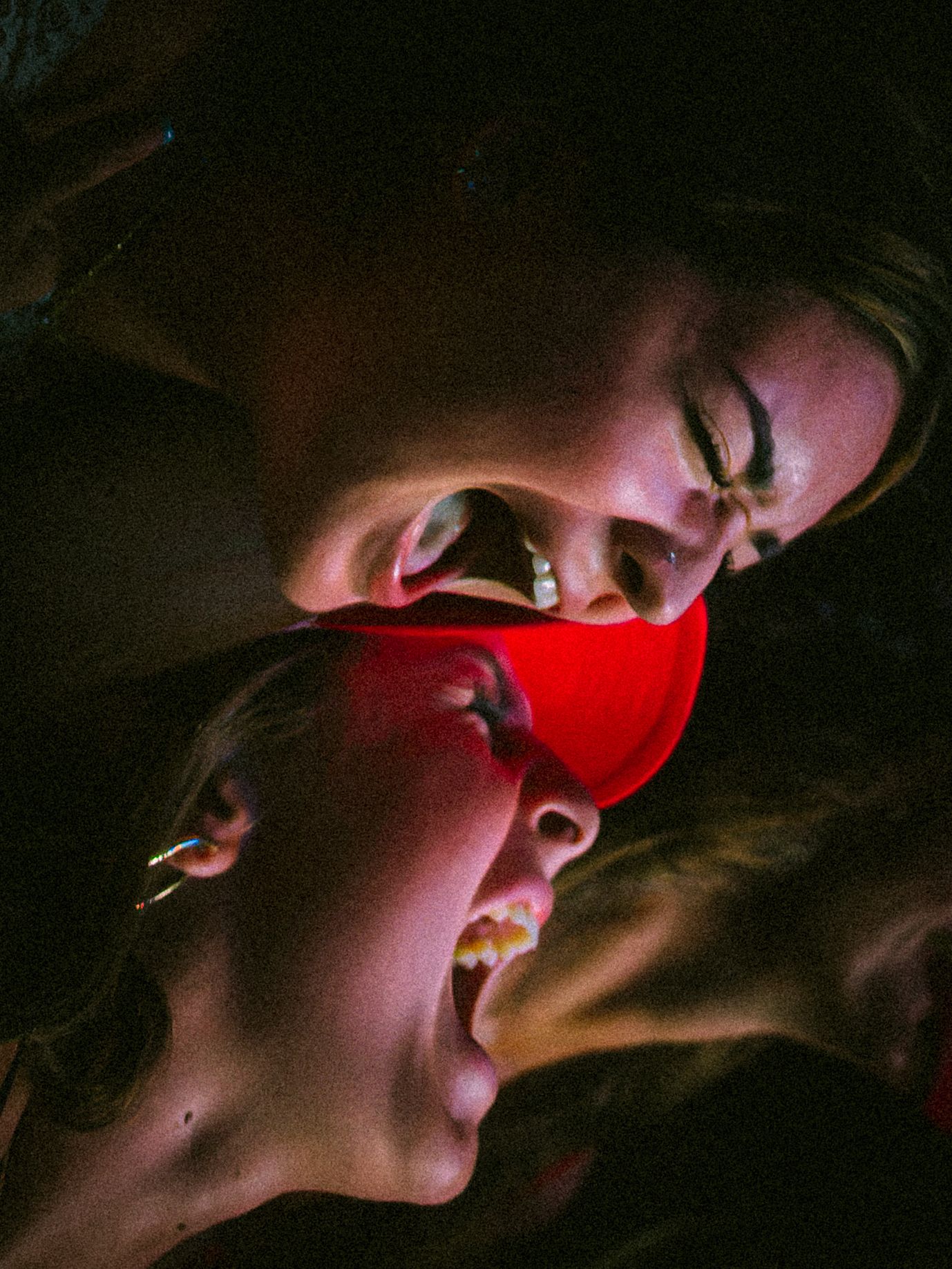 Two people with open mouths illuminated by red light in a dramatic, dark artistic portrait photo.