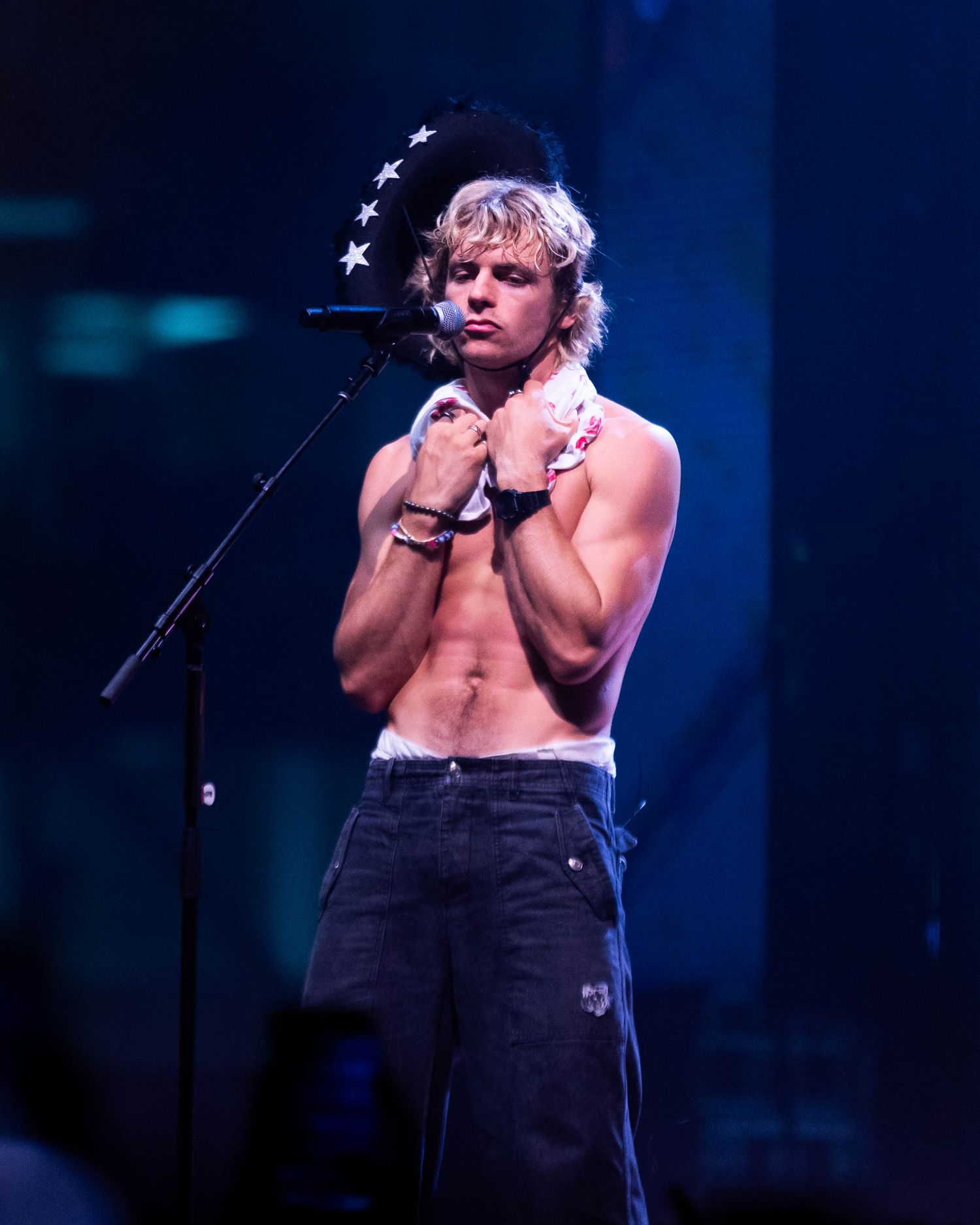 Performer on stage with microphone against blue theatrical lighting.
