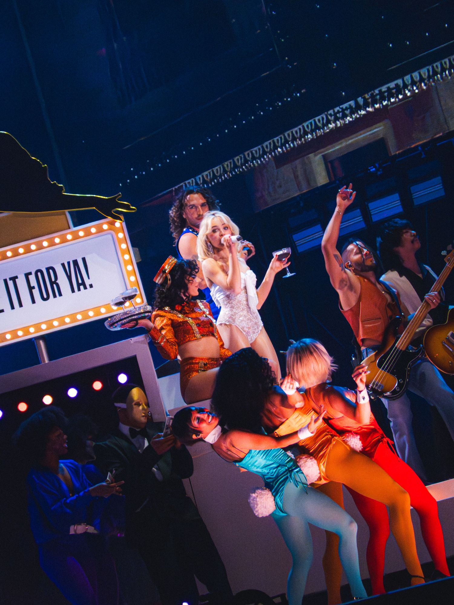 Energetic Broadway musical performance with colorful dancers on stage under marquee lights spelling IT FOR YA.