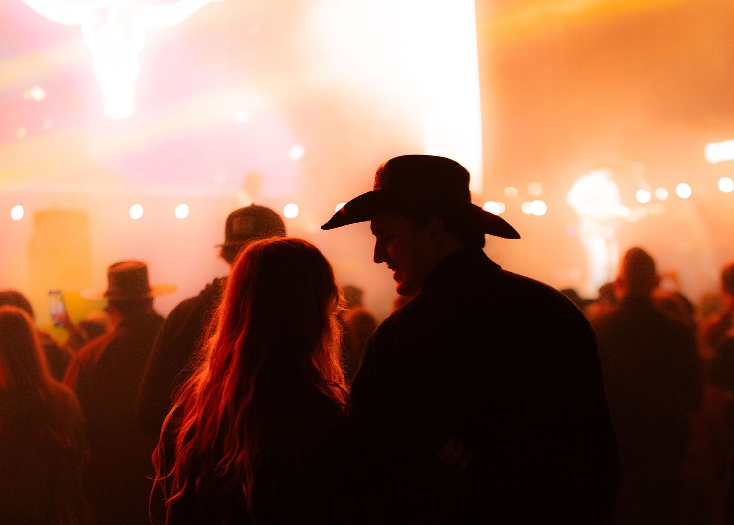 Silhouetted crowd against warm orange sunset lighting at an outdoor music festival.