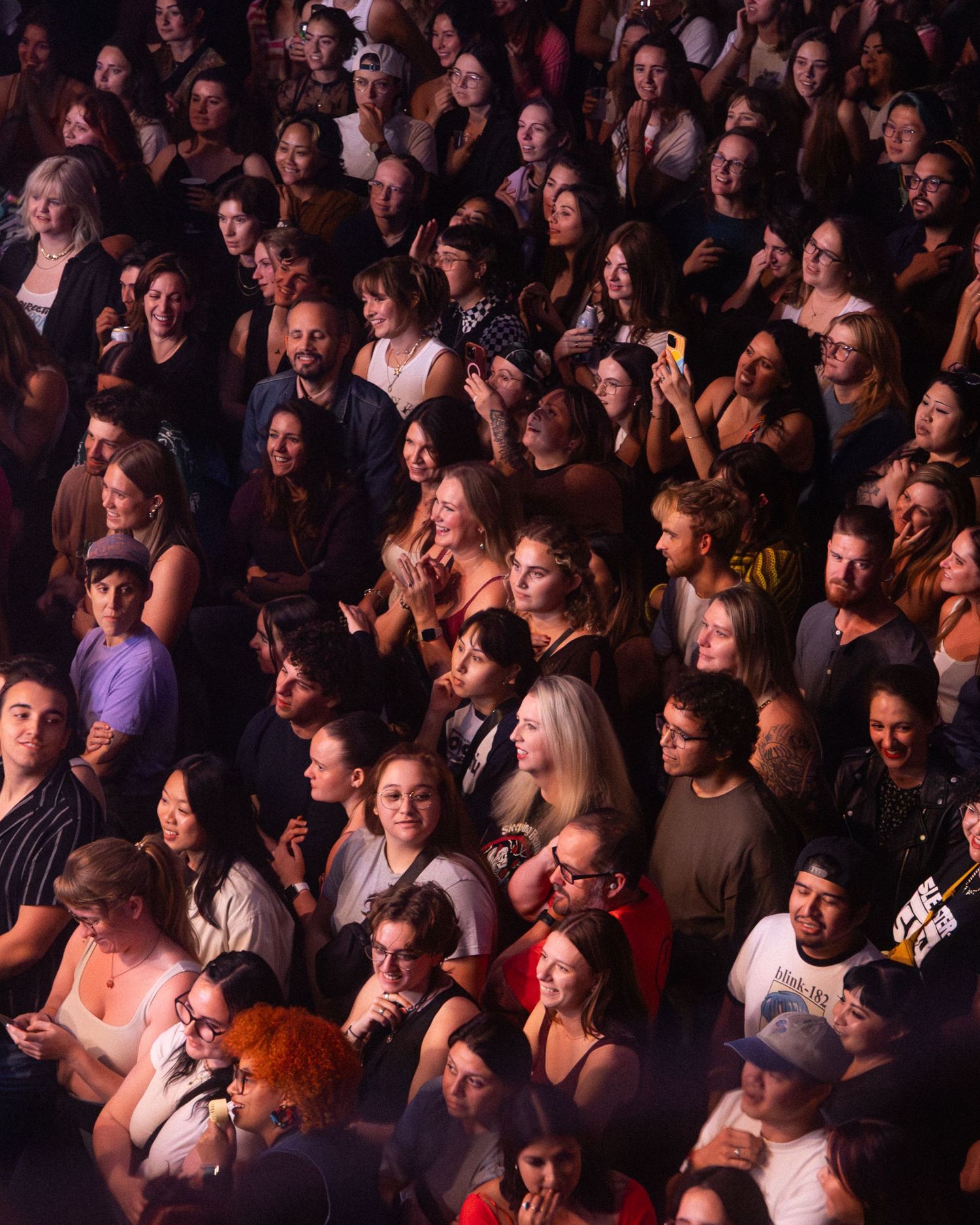 Large crowd of concert attendees packed together watching a performance in dim lighting.