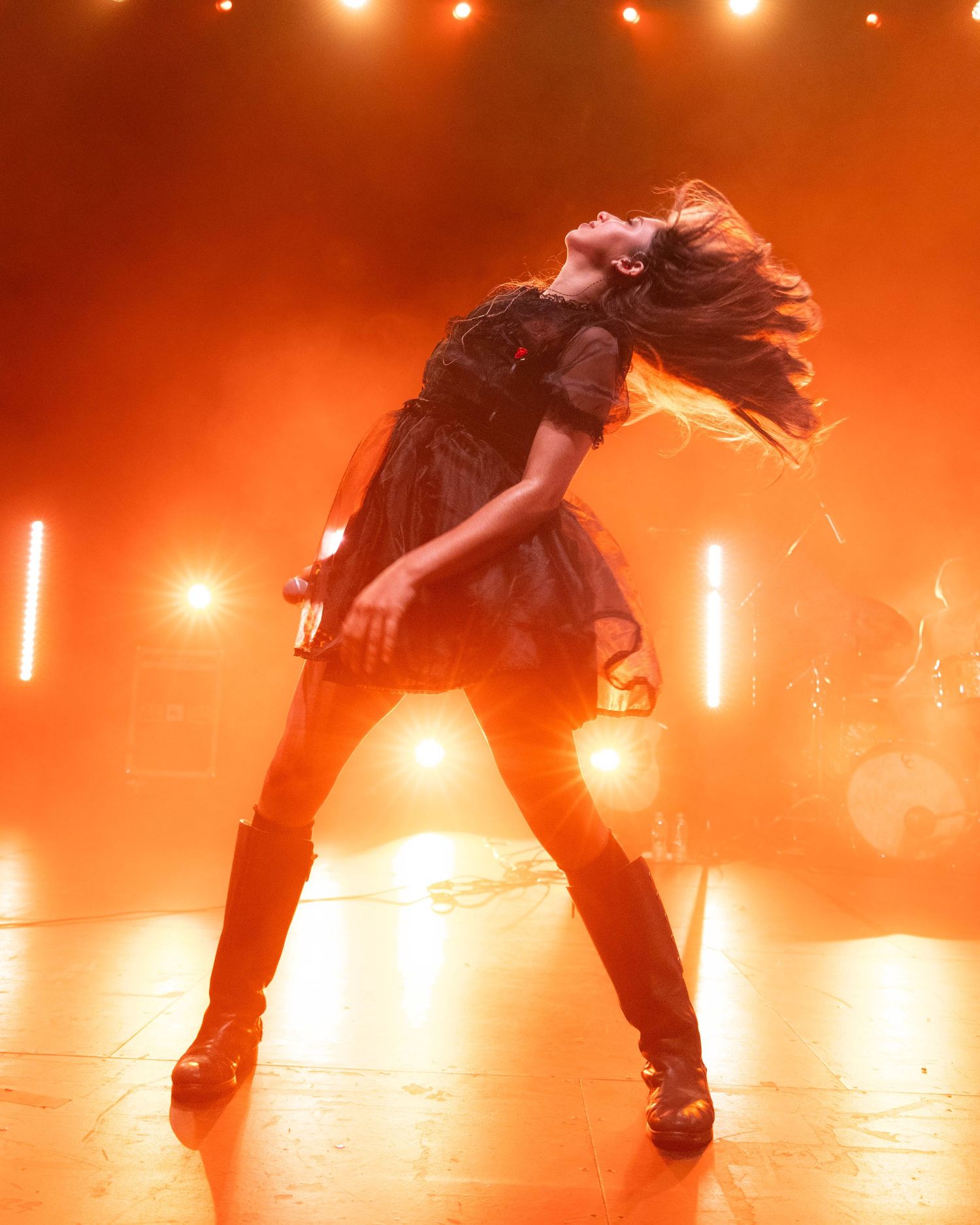Dramatic performance shot of dancer in dress silhouetted against orange stage lighting.