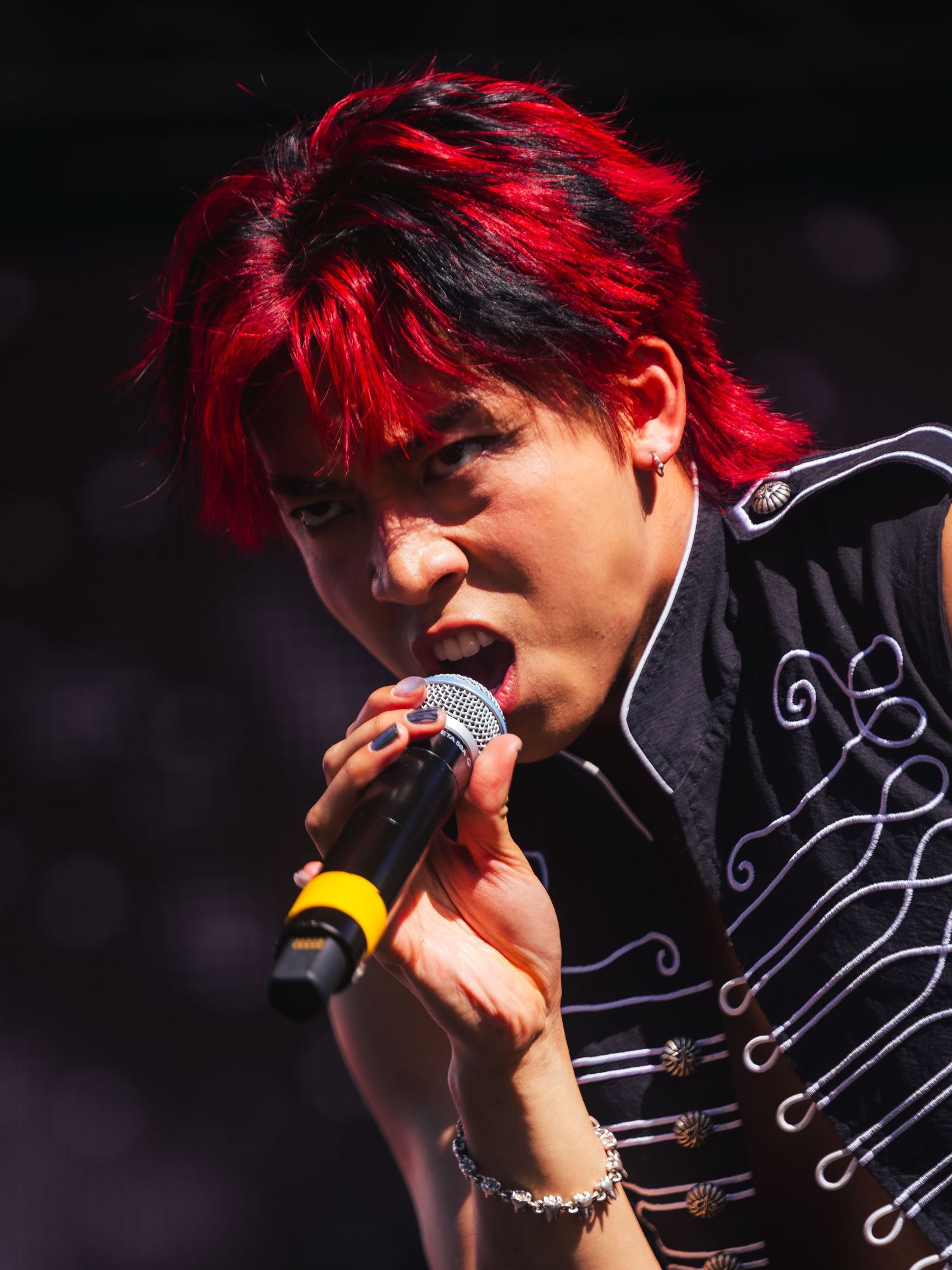 Young performer with vibrant red and black hair singing passionately into a microphone on stage.