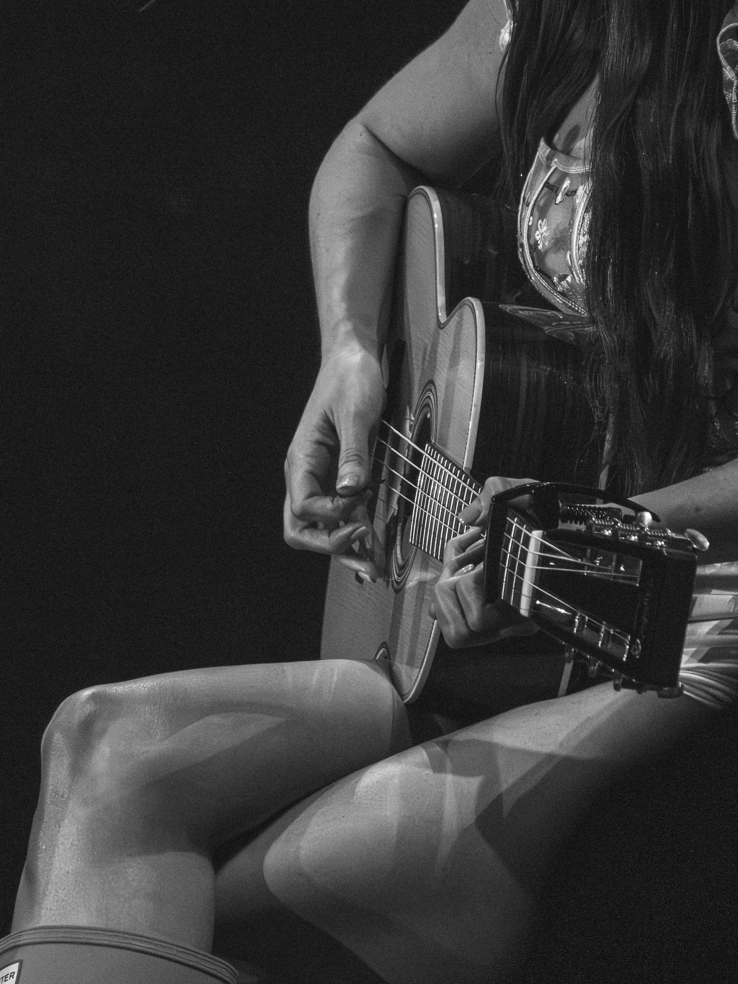 Close-up black and white shot of hands playing an acoustic guitar with intricate finger placement.