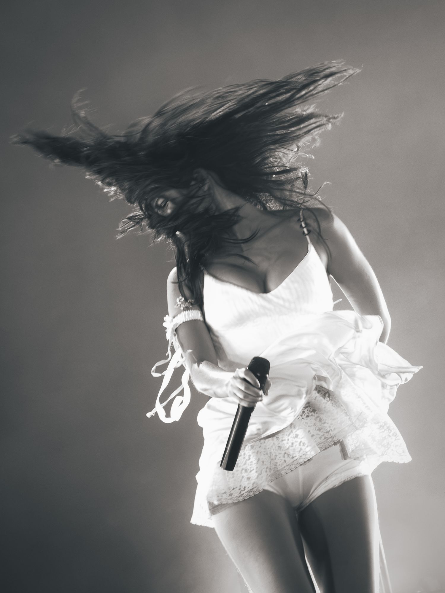 Black and white photo of a female singer performing on stage, hair flying, holding a microphone in a white outfit.