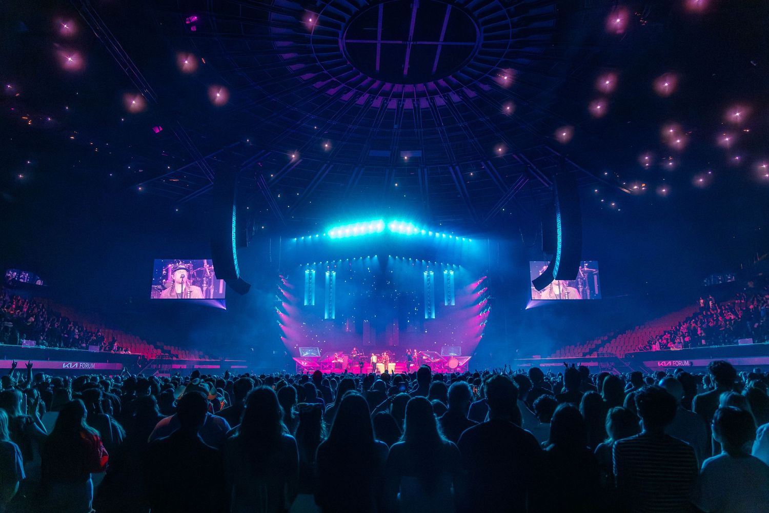 Large concert arena with vibrant pink and blue lighting effects illuminating a packed audience.