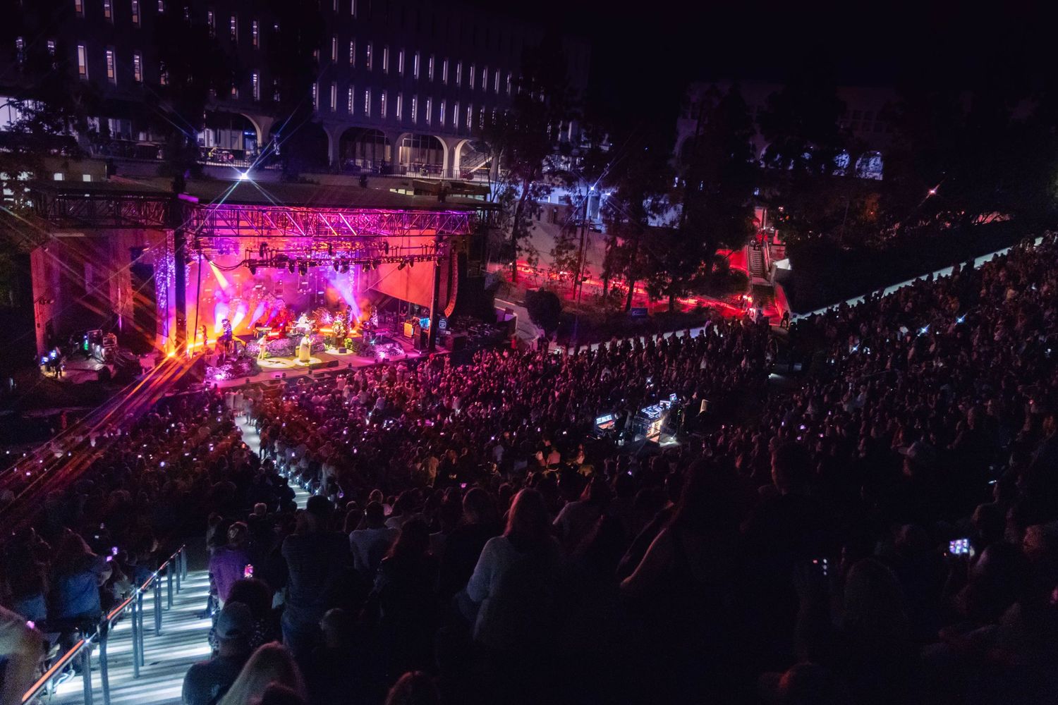 Large concert venue bathed in purple lighting with crowd watching performers on stage.