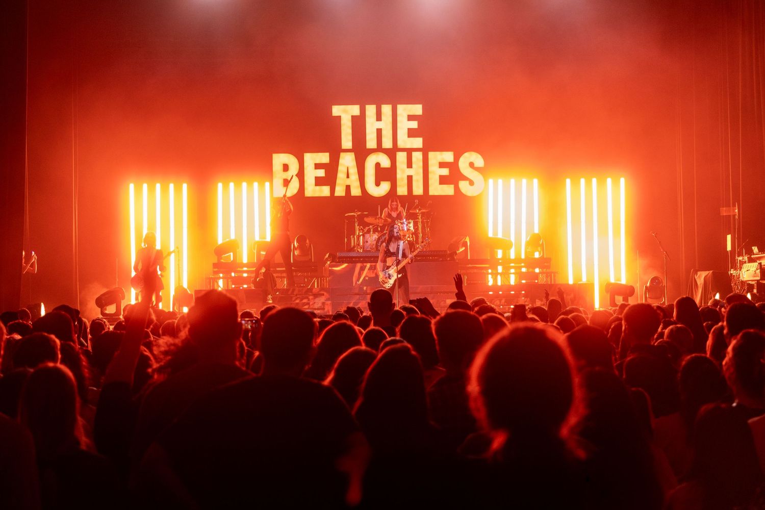 Concert crowd silhouetted against red stage lighting with illuminated 'The Beaches' sign.