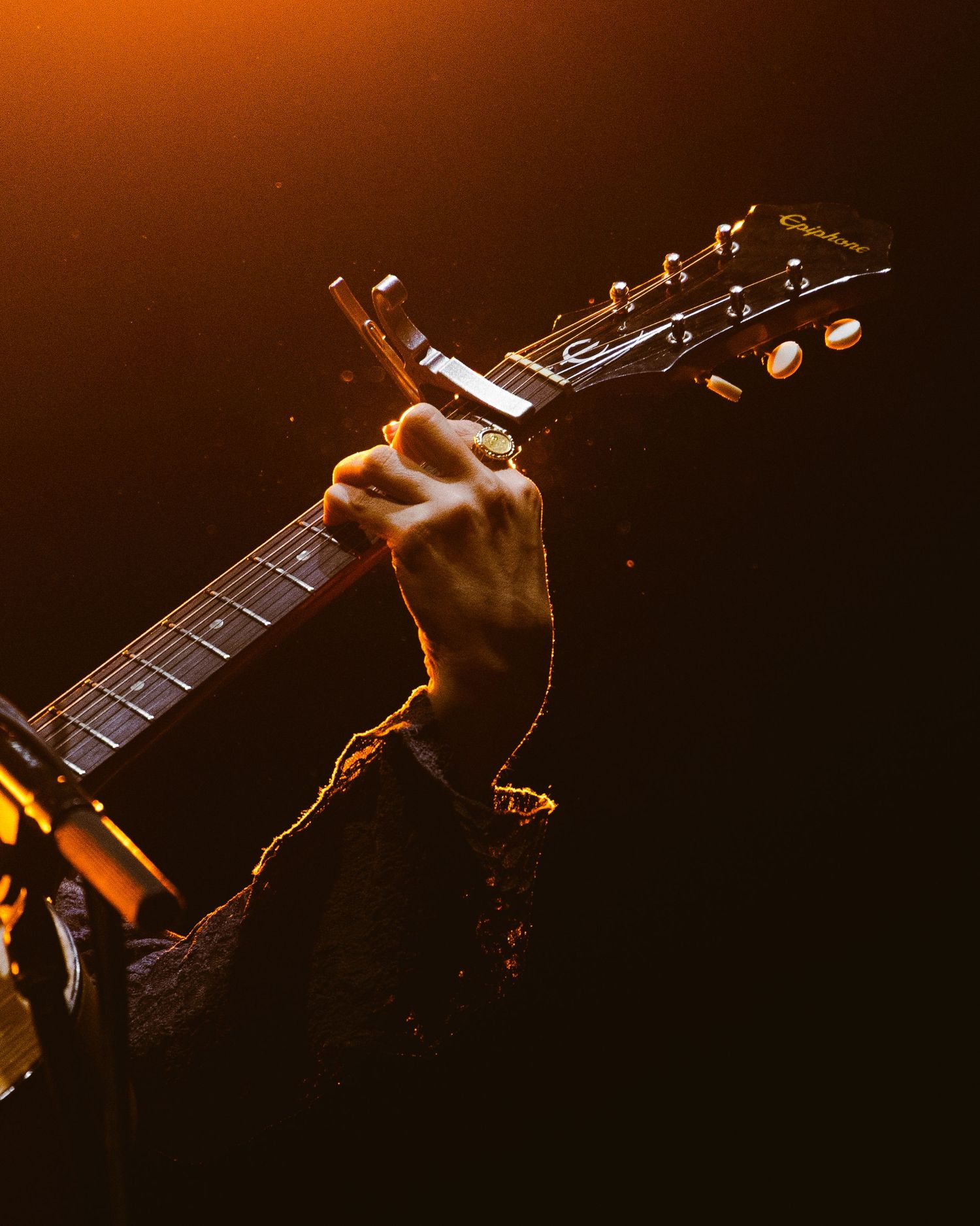 Close-up silhouette of hands playing an electric guitar on stage in dramatic lighting.
