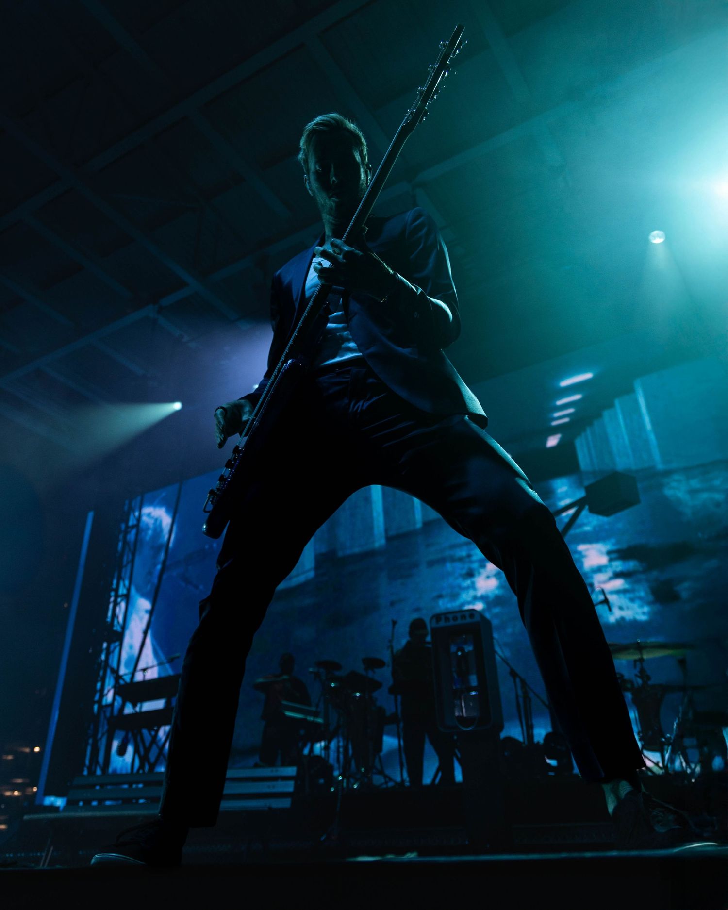 Silhouetted guitarist performing on stage backlit by dramatic teal lighting.