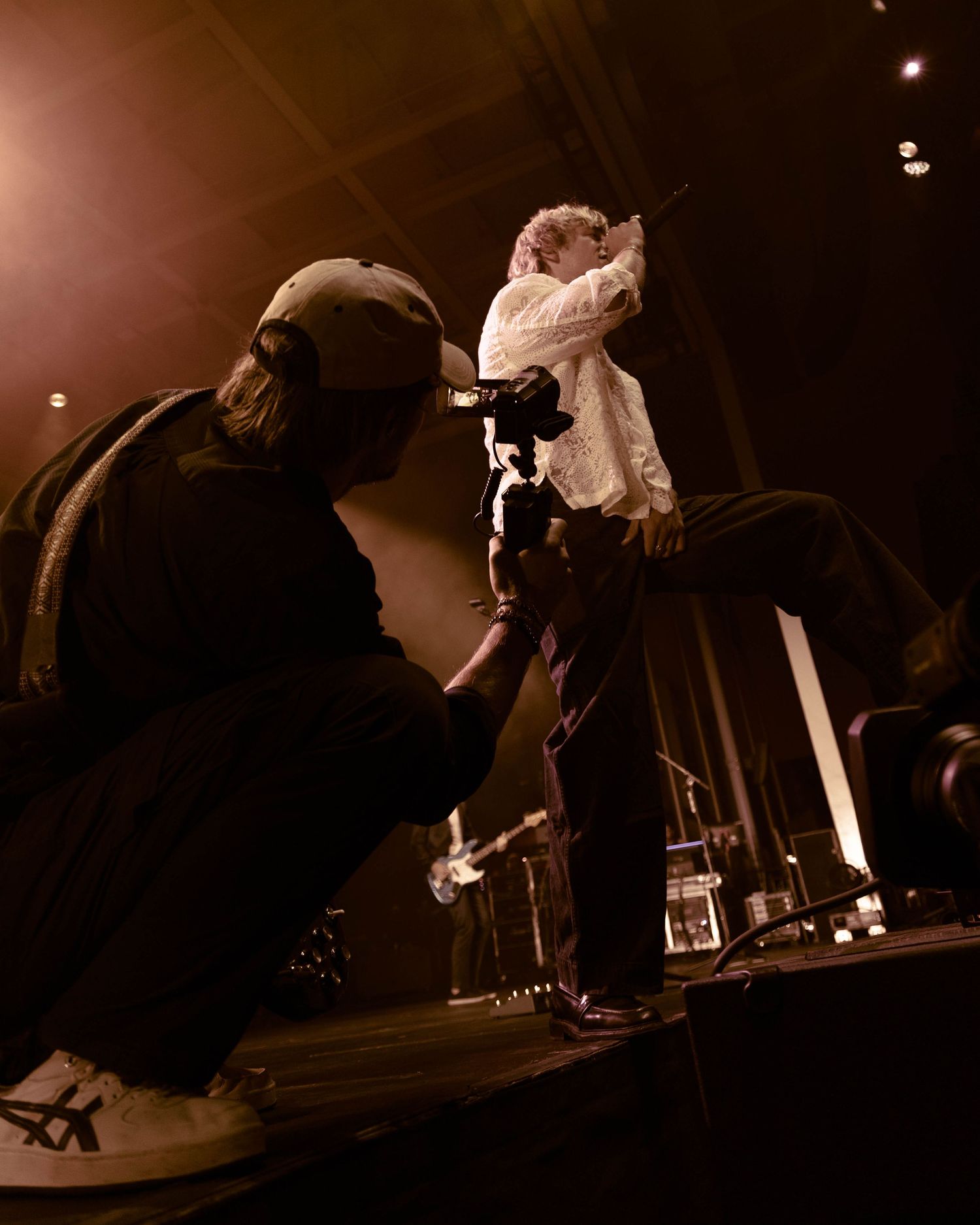 Camera operator filming performer on stage in dramatic sepia-toned lighting.