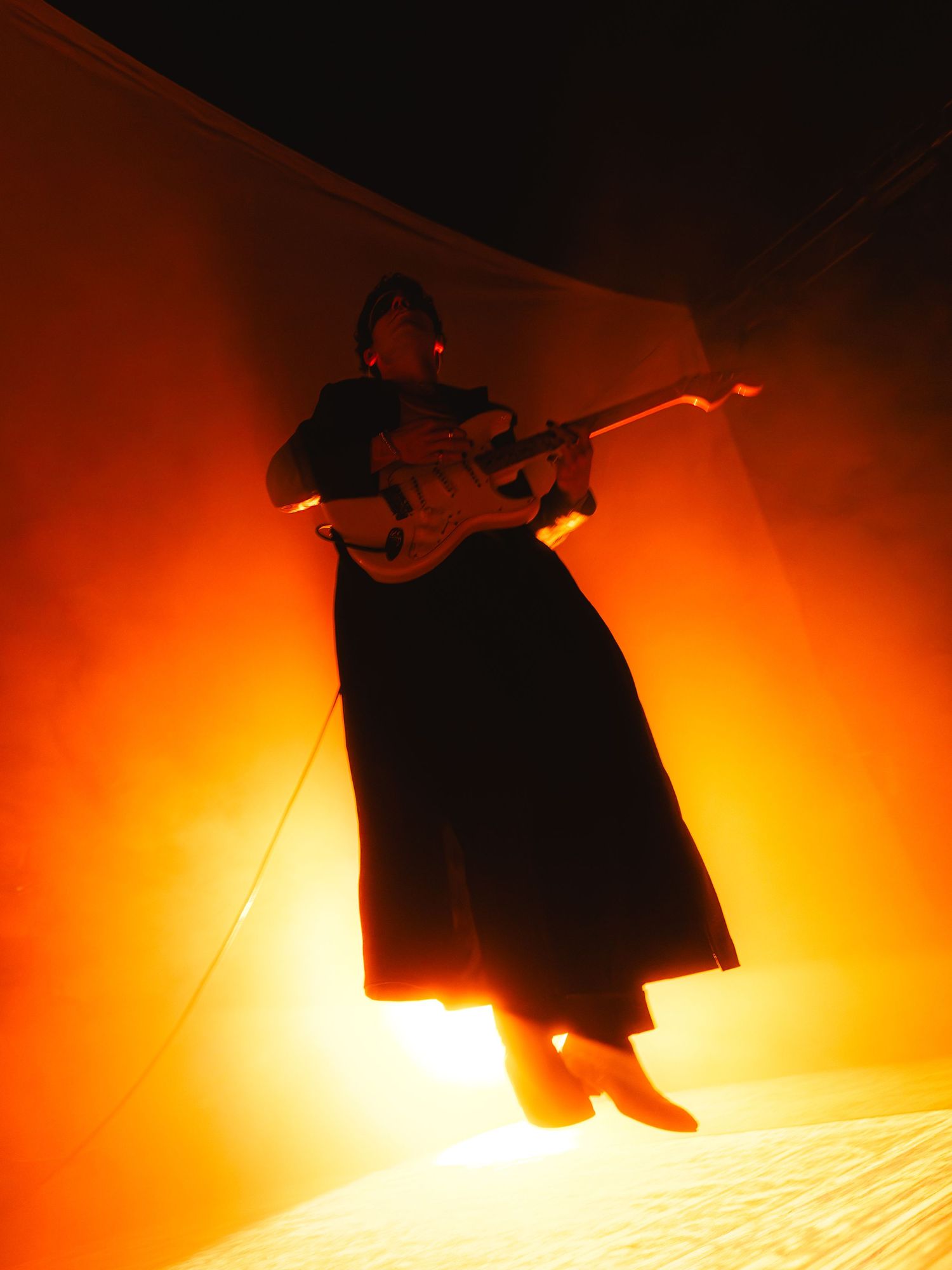 Silhouette of a figure suspended in mid-air against a dramatic orange and black background creating a theatrical effect.