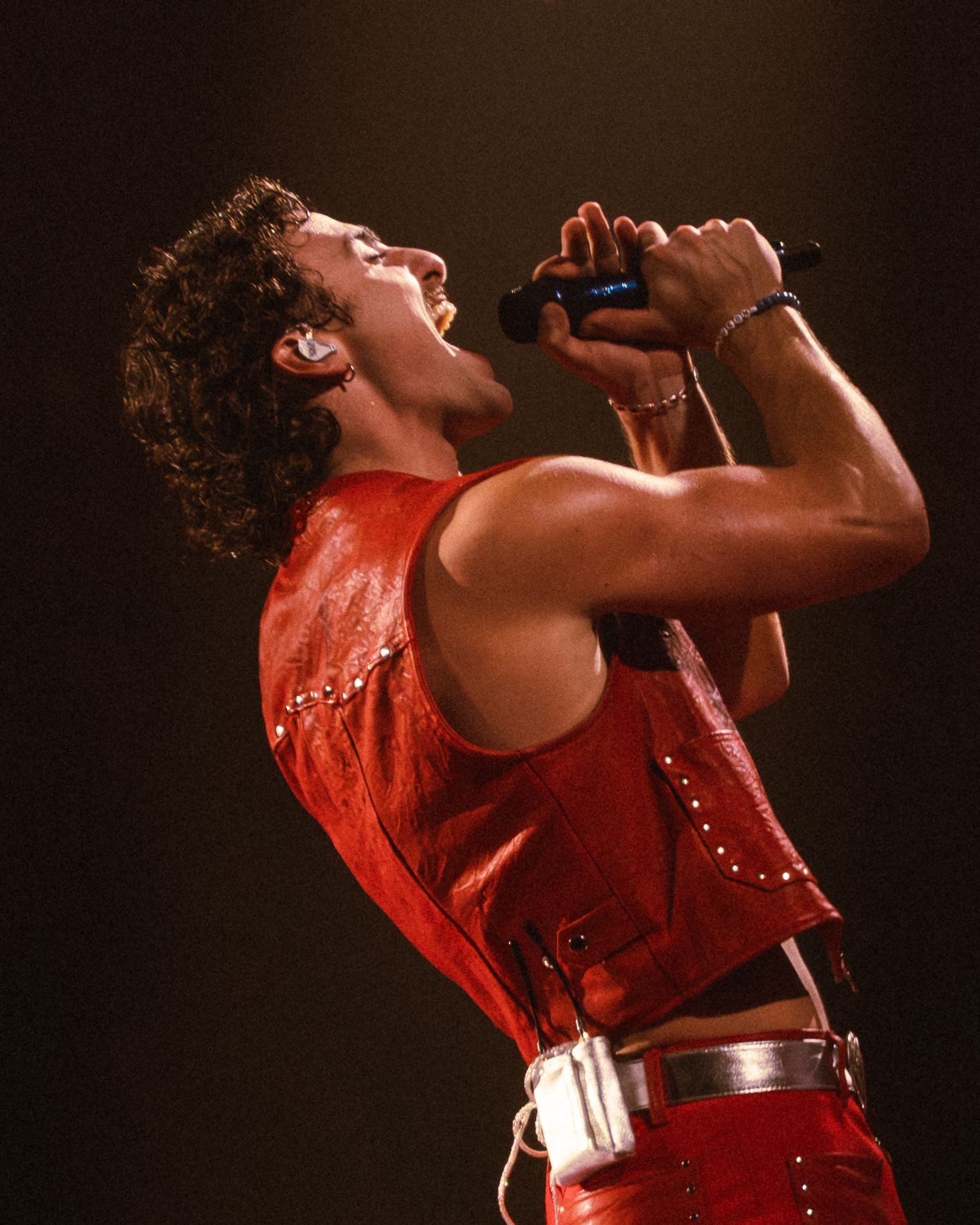 Performer in a red outfit singing passionately on stage during a concert performance.