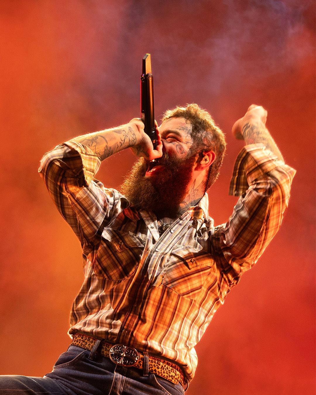 Musician performing energetically in orange stage lighting with dramatic smoke effects.