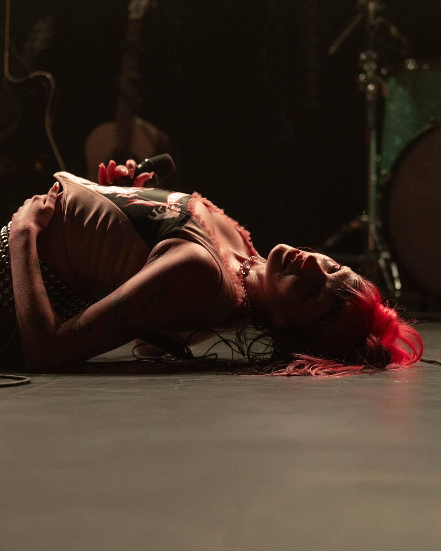 Performer lies on dark stage illuminated by dramatic red lighting.