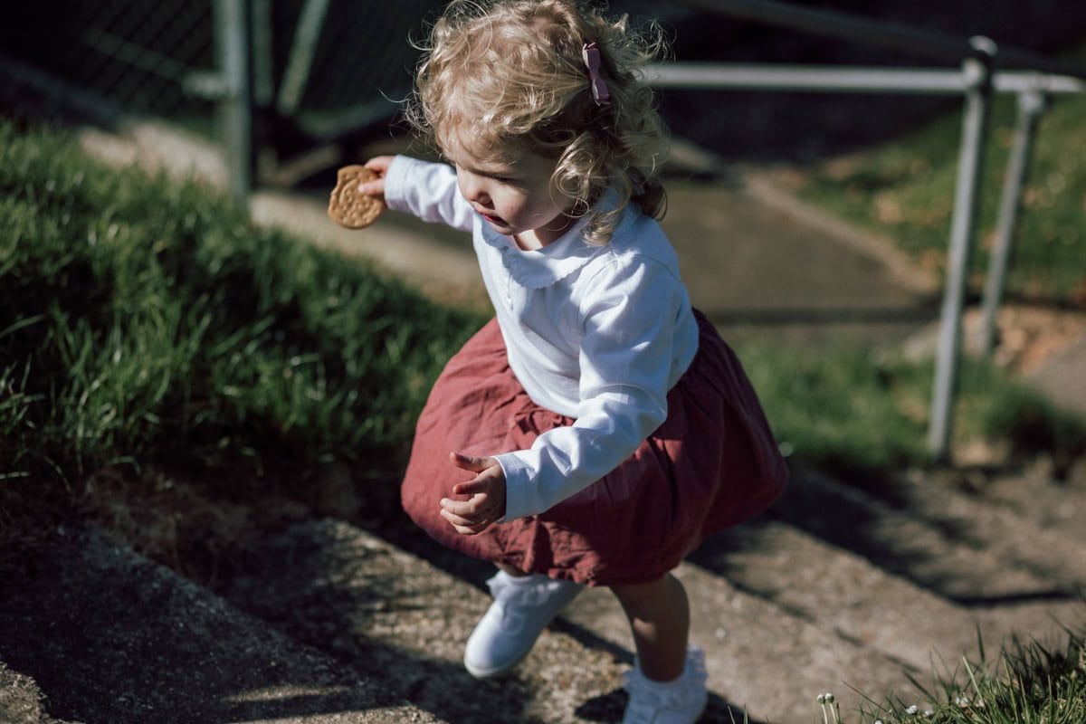 A little girl clutching a biscuit as she climbs some steps.