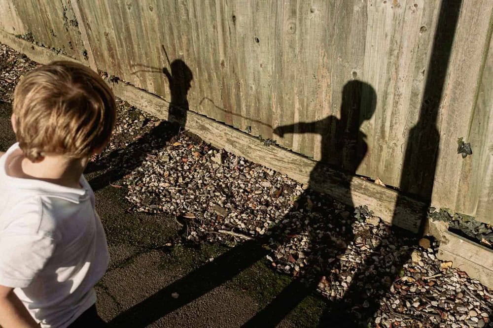Two boys play at swordfighting - their shadows shown on the fence.
