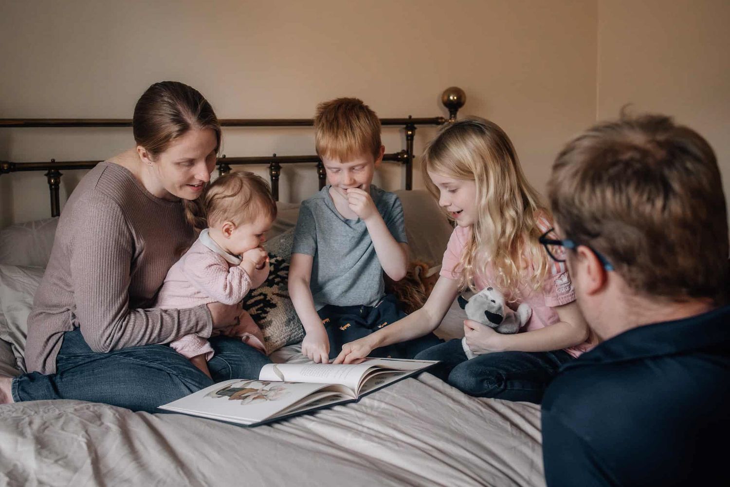 A family of five reading together at home on a double bed.