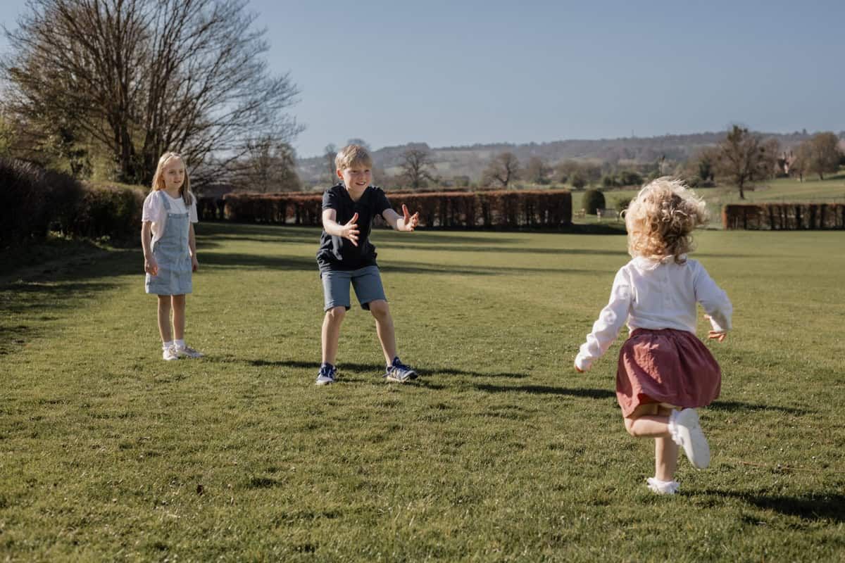 A boy holds out his arms, encouraging his young sister to run towards him.