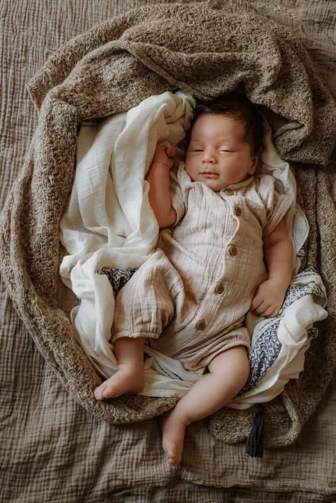 A baby lies in a nest of blankets on his parent's bed.