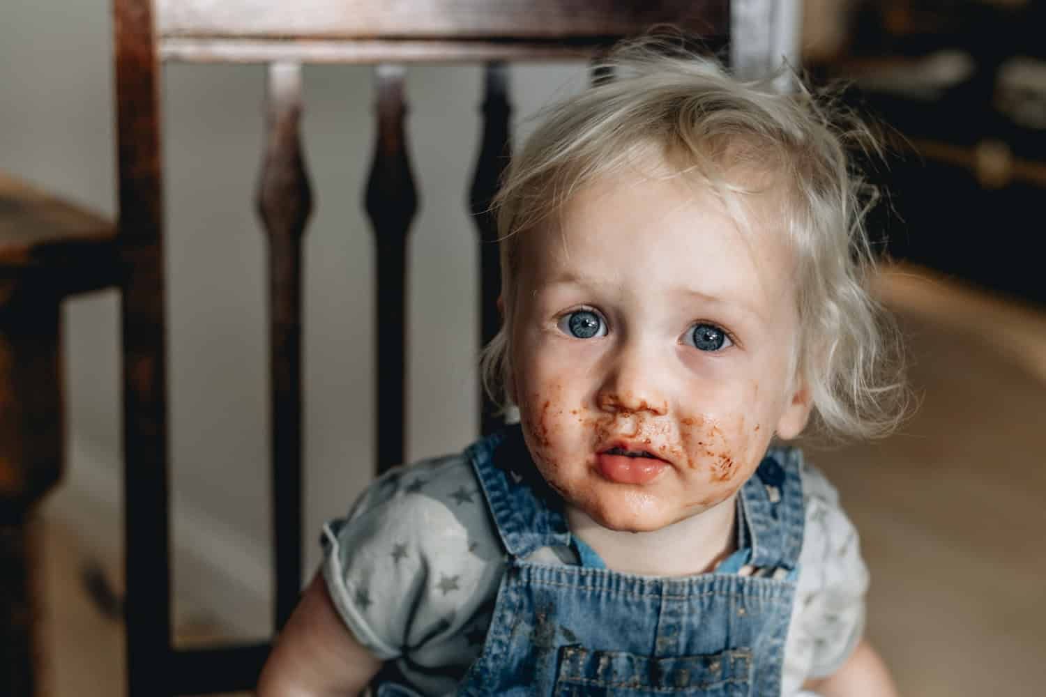 A toddler looks to camera, his face covered in chocolate.