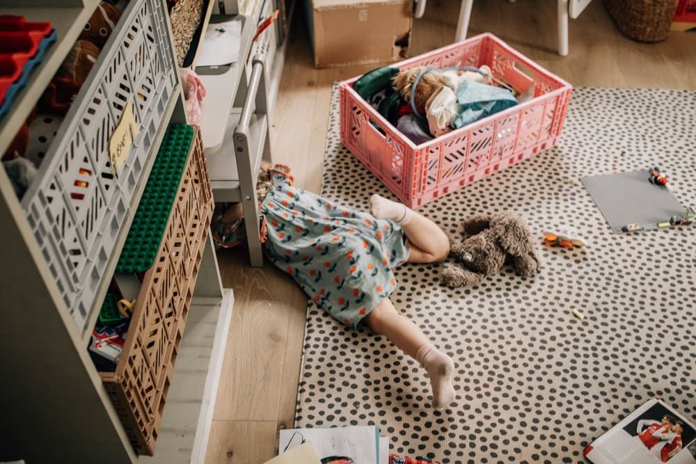 A young girl has dived under a table during an in-home family session in Marlow- her legs stick out from beneath the table.