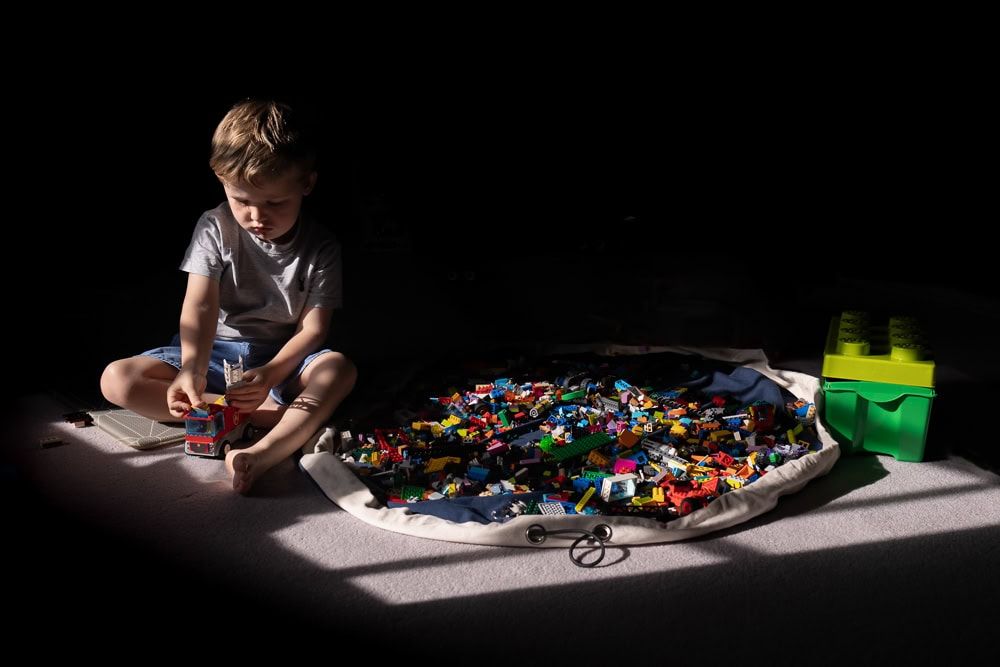 A young boy playing Lego in a patch of window light.
