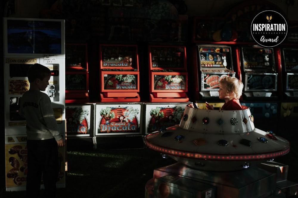 An inspiration award badge on a photograph of two children playing in a seaside arcade.
