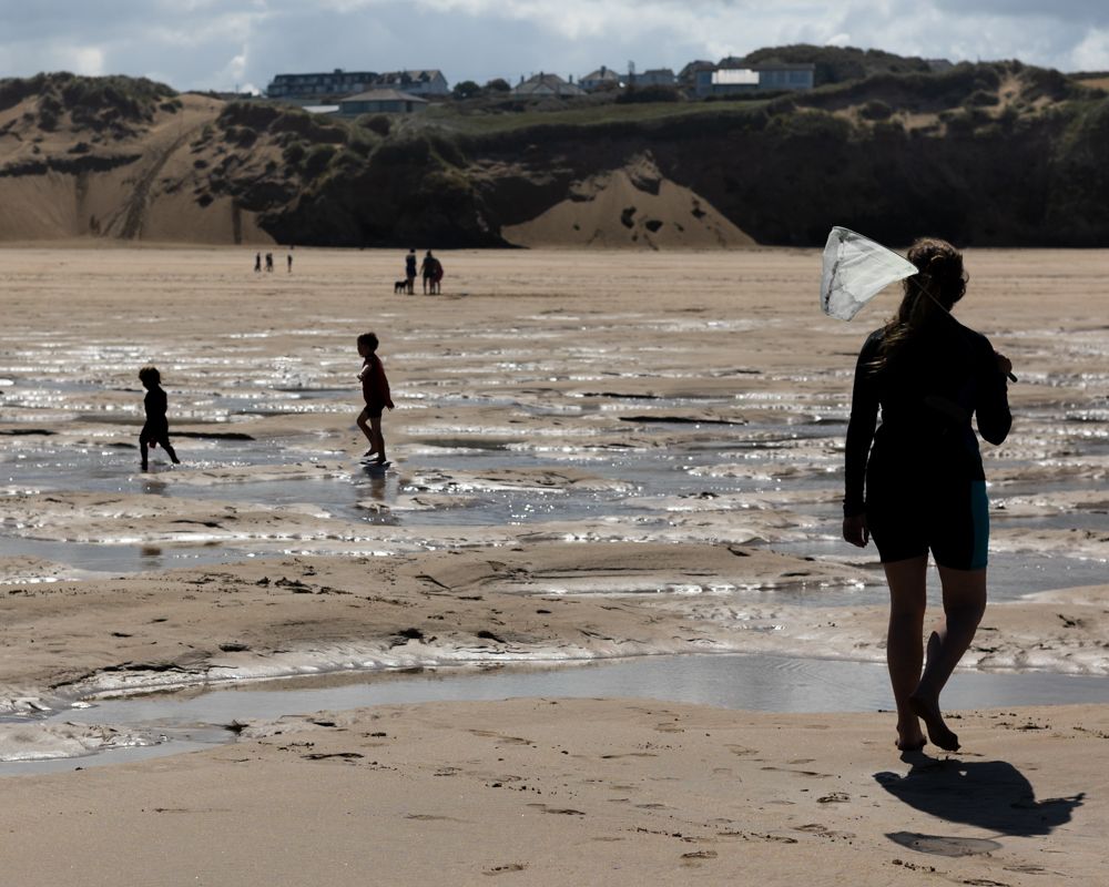 Silhouettes of a mum carrying a fishing net walking up a beach after her children.