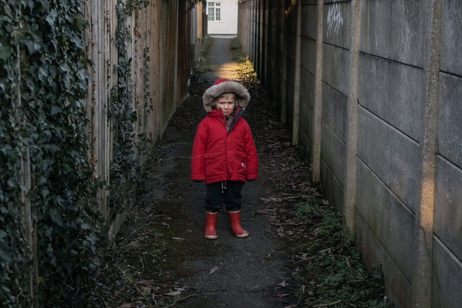A child stands still with a grumpy pout on his face in an alleyway.  He is clearly unimpressed with the walk.