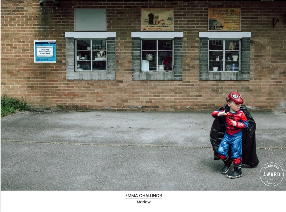 A young boy dressed as spiderman carries a black bag full of balloons pasted three small windows.