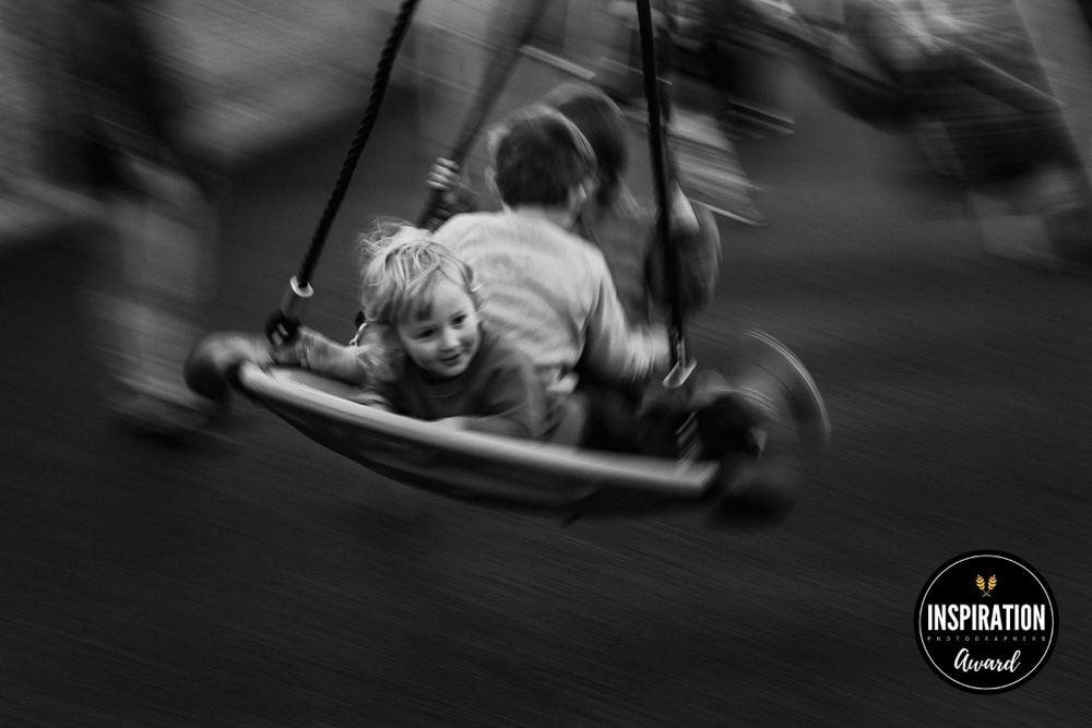 Three boys ride on a big swing, a panning technique shows the feeling of their movement.