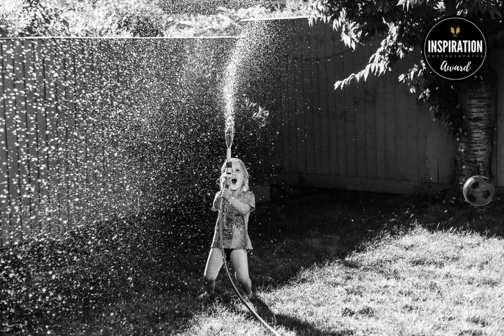 A young boy looks joyful as he squirts a hosepipe up in the air in a garden in Marlow.