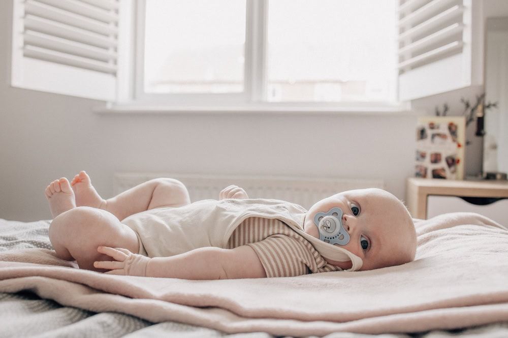 A baby lies on his parent's bed,looking at the camera.