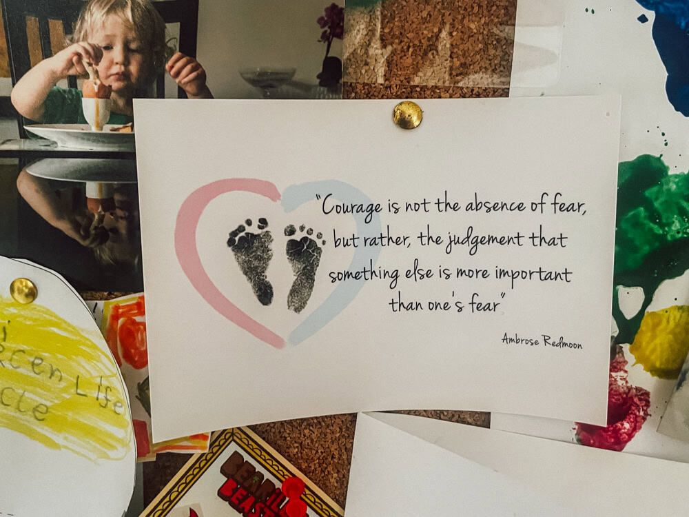 A photograph of a postcard on a noticeboard.  Next to a baby's footprints in a heart, it reads 