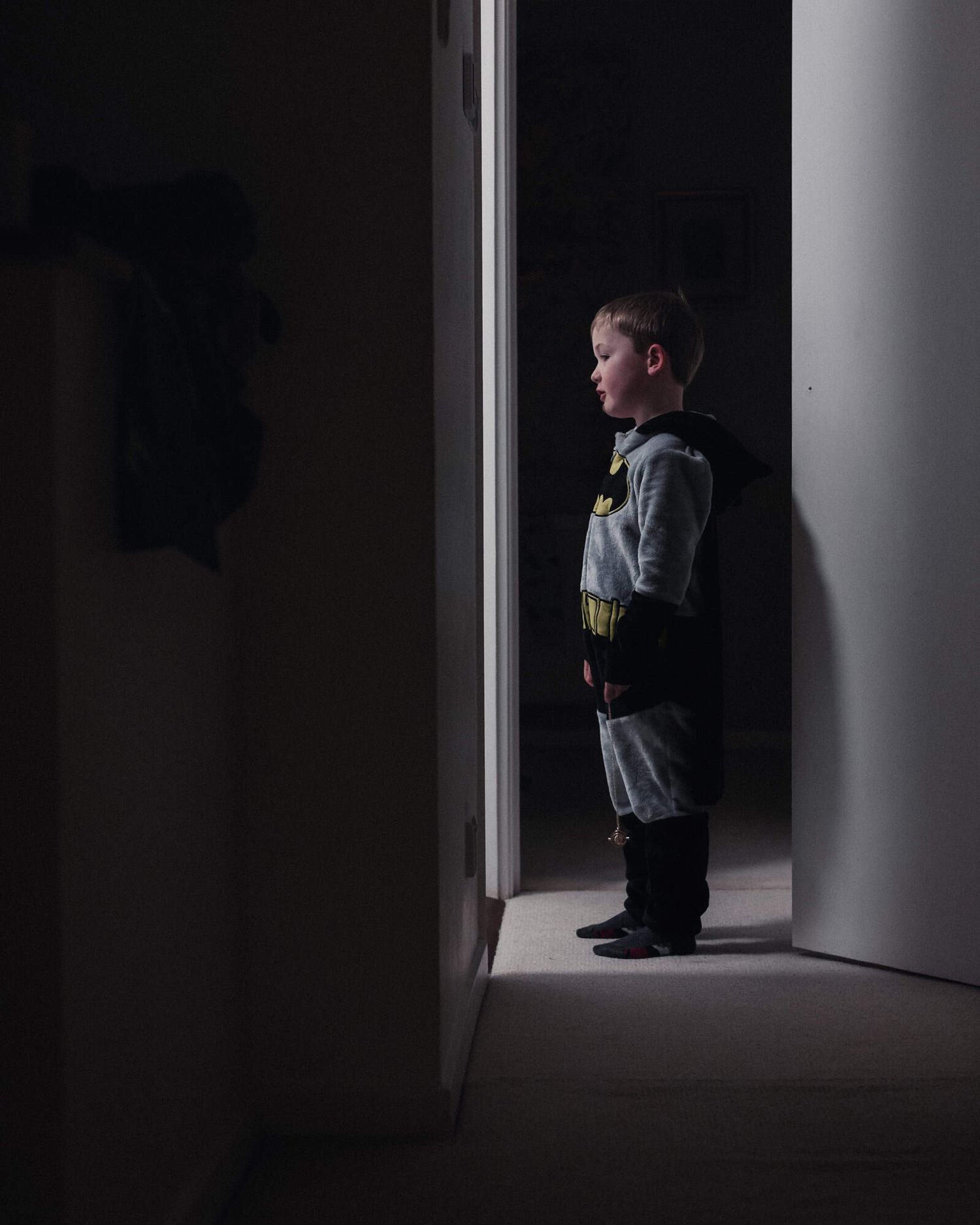 A young boy wearing a batman outfit illuminated in a dark corridor.
