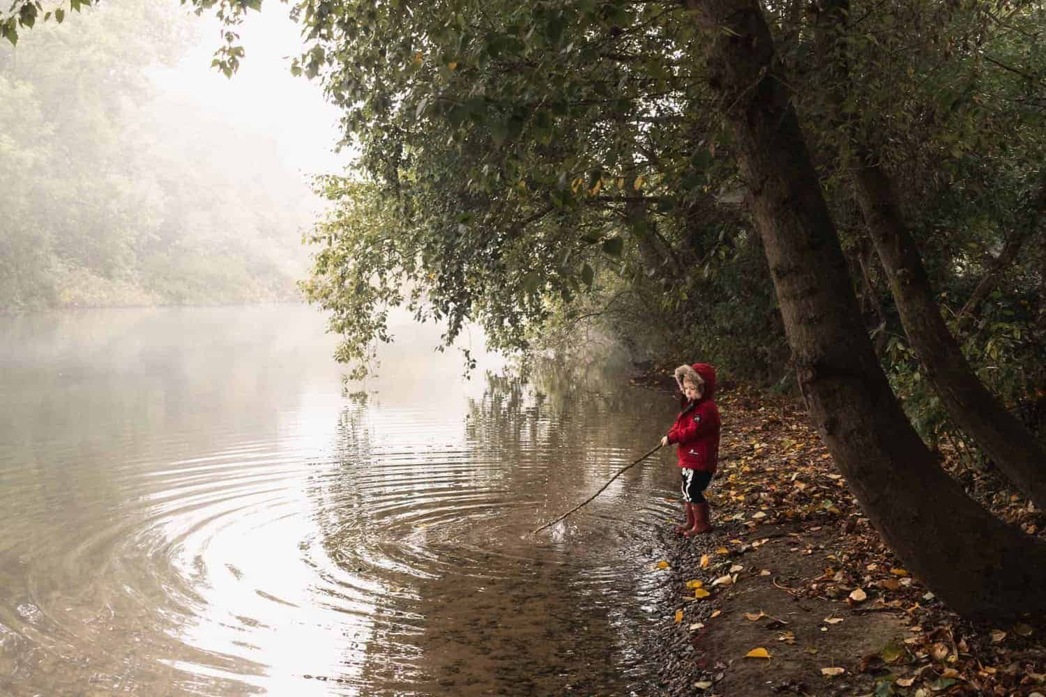 A child using a stick to pretend to fish in the river near Dorney in Maidenhead.