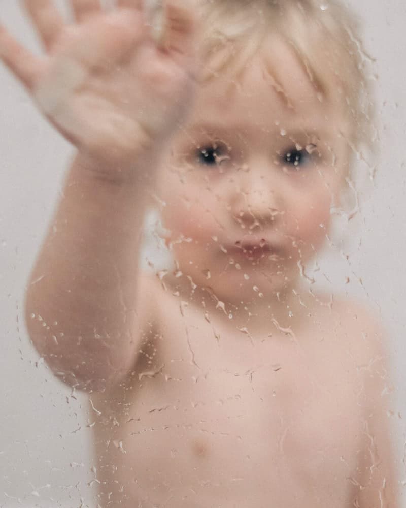 A child wipes the shower screen in the bath.